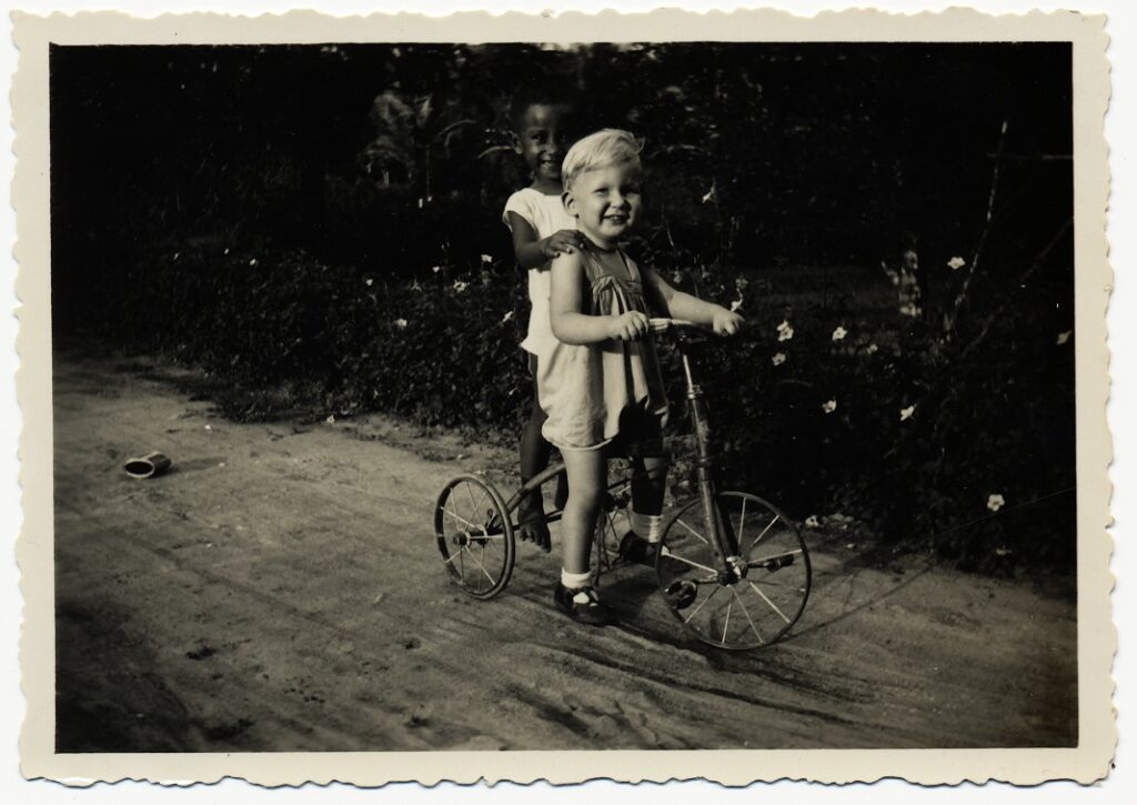 View the photos 1 van Onbekend: Europees jongetje op een driewieler met een inheems kind, ca. 1935